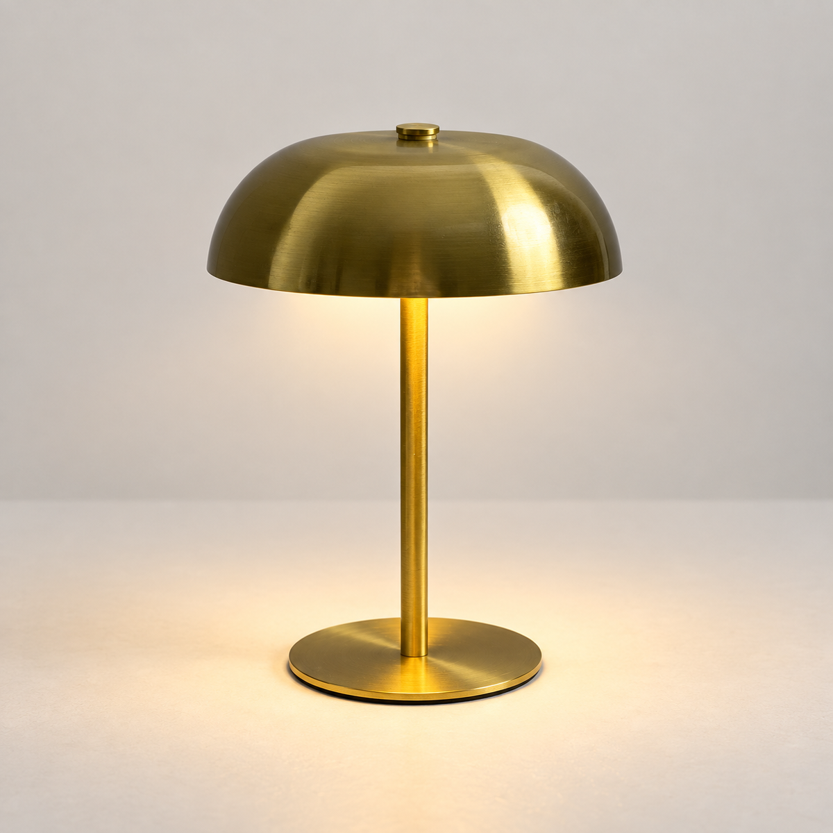 Compact brushed gold mushroom touch lamp switched on in a light studio