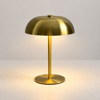 Compact brushed gold mushroom touch lamp switched on in a light studio