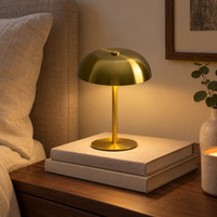 Brushed gold cordless mushroom lamp on stacked books beside a bed