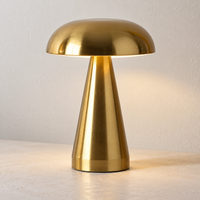 Gold cordless mushroom touch lamp with conical body switched on against a light wall