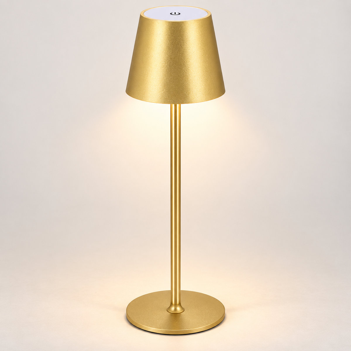 Gold-tone frame cordless touch table lamp switched on against a light wall