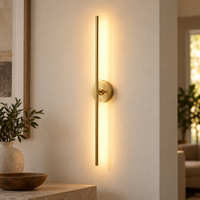 Gold cordless vertical bar wall light mounted and switched on against a light wall