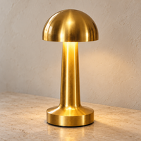 Rounded gold cordless mushroom touch lamp switched on against a light wall