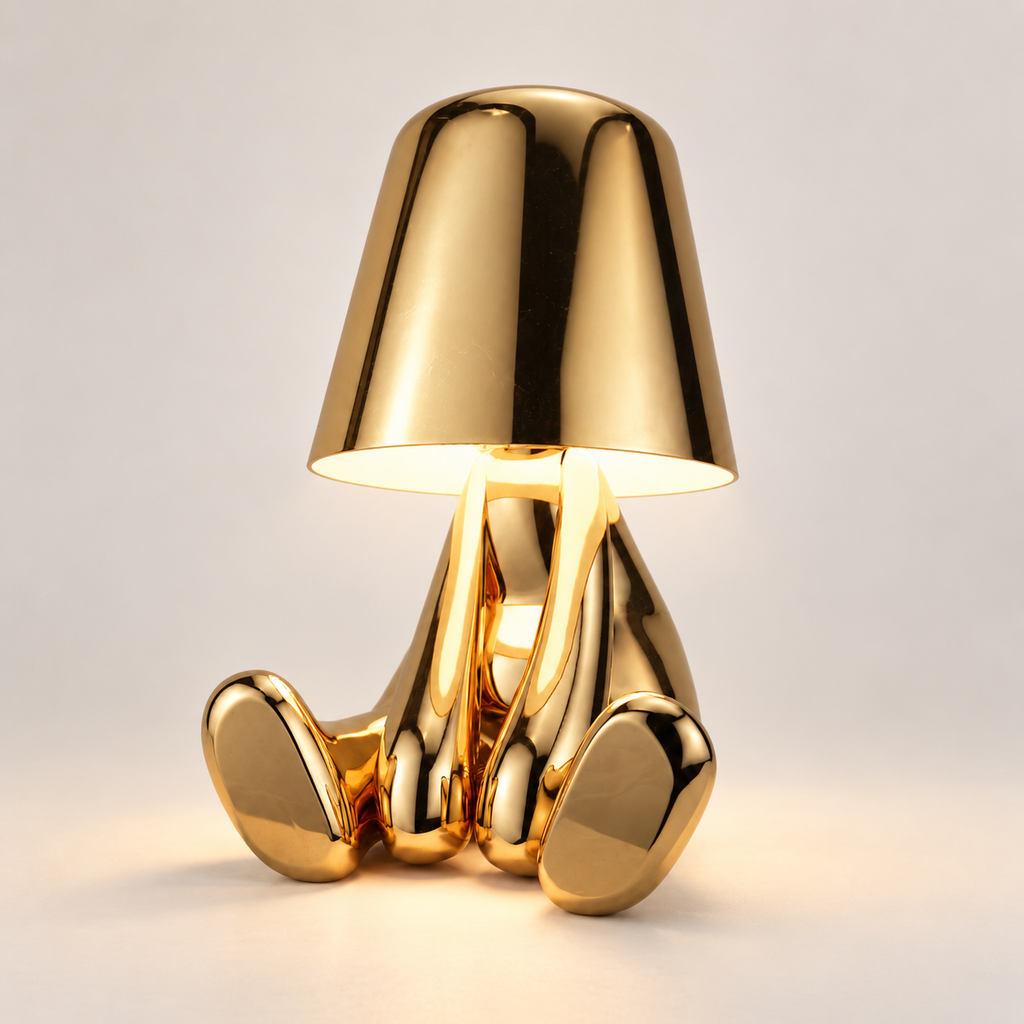 Gold seated figure rechargeable table lamp switched on in a light studio setting