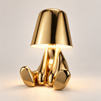 Gold seated figure rechargeable table lamp switched on in a light studio setting