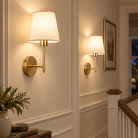 Two gold cordless wall sconces illuminating a cream hallway