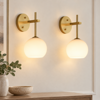 Set of two gold wall lights with frosted glass globes switched on