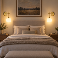 Pair of gold glass globe wall lights mounted beside a neutral bed