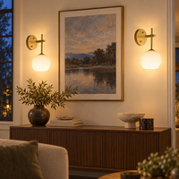 Two gold globe wall sconces illuminating artwork above a walnut console